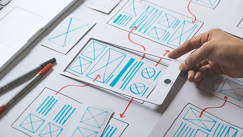 Hand legt Skizze eines App-Entwurfs auf einen Tisch